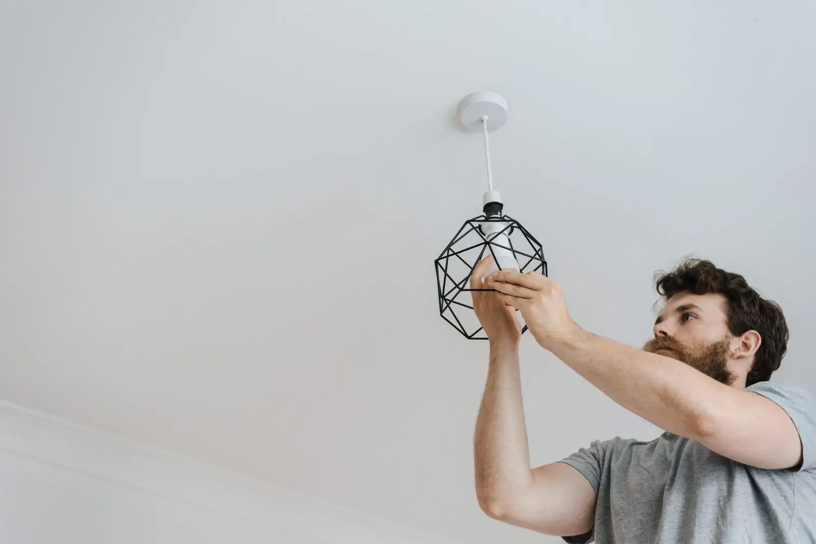 Man reaching up to a wire-cage pendant light hanging from a white ceiling